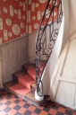 Vue de l'escalier tournant en bois avec rampe en fer forgé.