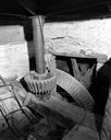 Détail de la transmission du vieux moulin : l'arbre moteur (relié à la roue hydraulique située à l'ouest de l'autre côté du mur), le rouet de fosse, l'axe vertical et son pignon.